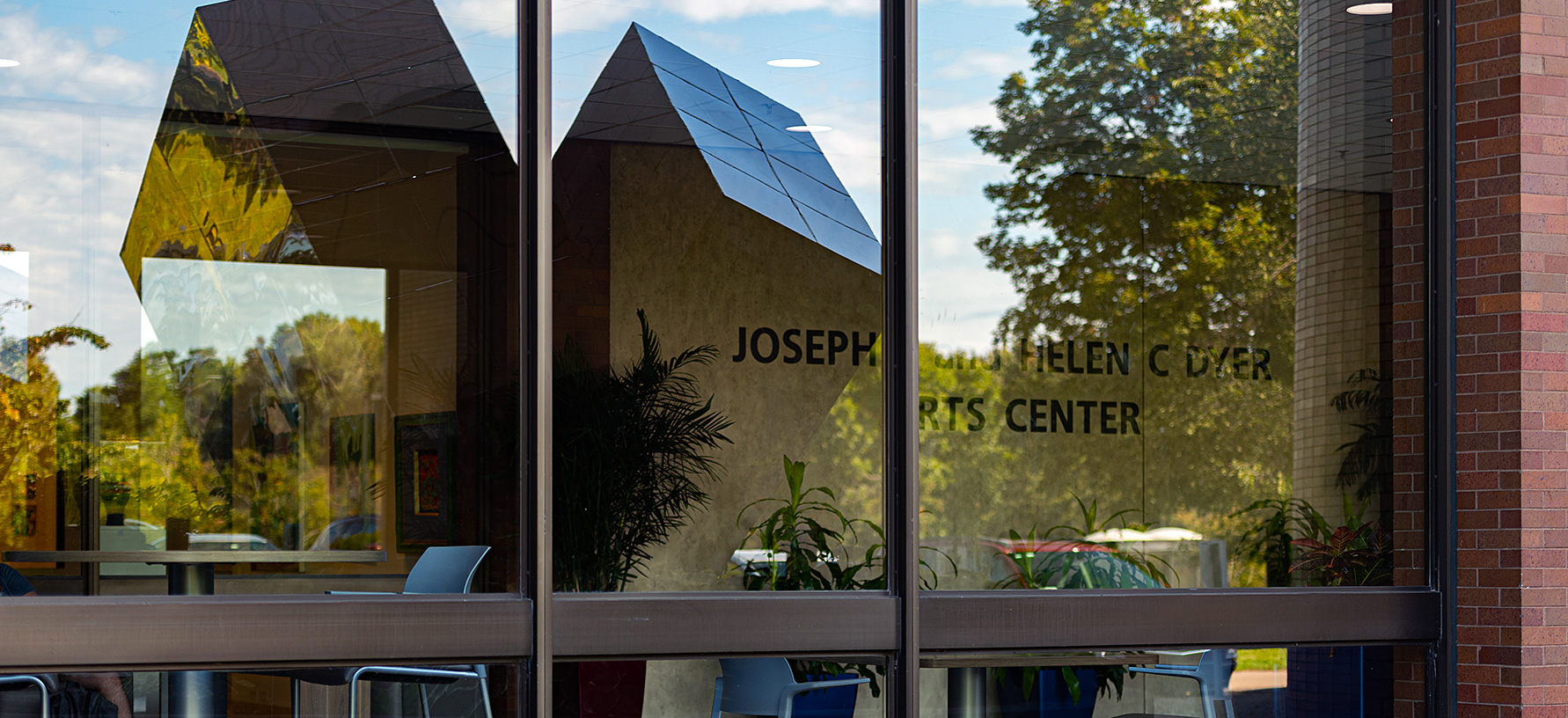 The Split Cube is reflected in the front window of Lyndon B Johnson Hall,  Sept 16, 2019. The cube, which is located on the north side of LBJ, was created by Carl Zollo to commemorate NTID's 10th anniversary in 1978.