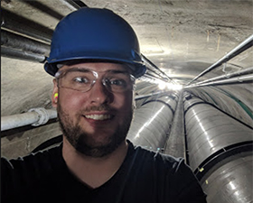 Photo of Ryan Koester, young man in industry tunnel setting wearing safety googles and hardhat