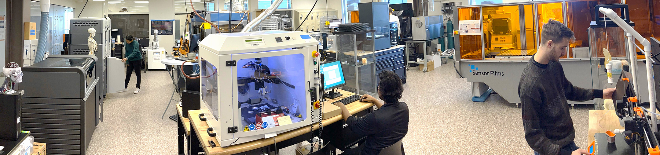 a panorama view of the AMPrint lab with three people working at different equipment