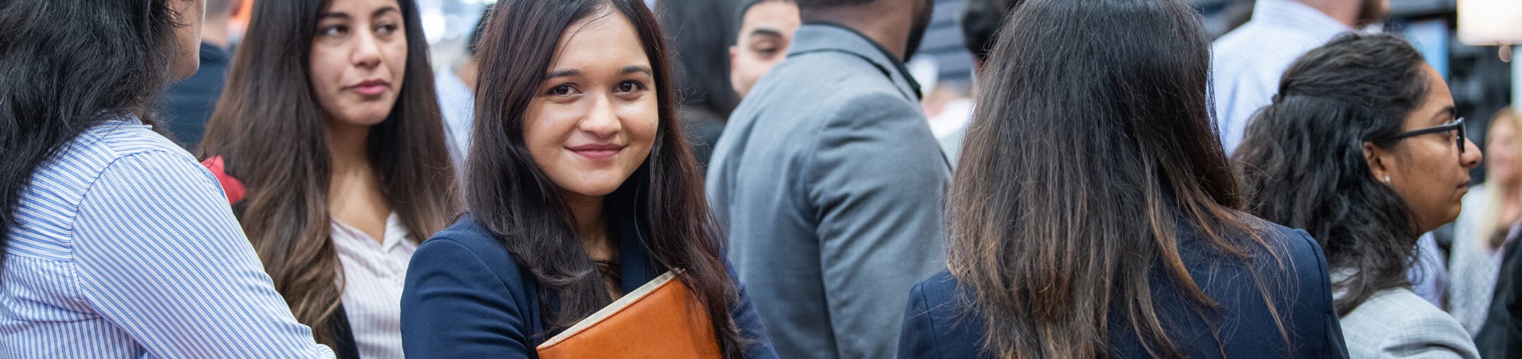 A Female RIT student holding a folder and standing in line at a career fair.