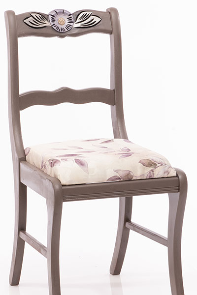 Dark gray chair with carved flower on chair back.  Flower painted purple.  Cream  color fabric seat with gold, gray and purple leaves design.