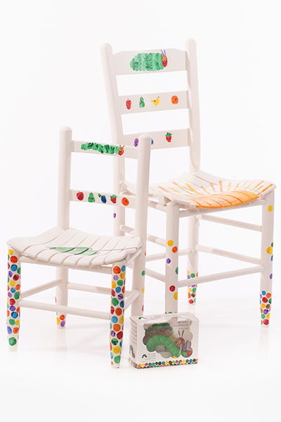 2 CHAIRS and 1 BOOK.  1 adult chair and 1 matching child's chair.  Both chairs have a white background with caterpillars and fruit on the back rungs.  There are colored dots on the legs and the back of both chairs, the adult chair has a large sun and the child chair has a green leaf with a tiny egg on it.