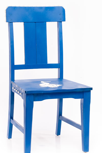 Blue Chair with a Stork standing inside a white rose. There are pearls spread across various sides of the chair. There are also little facts glued to the bottom of the chair.