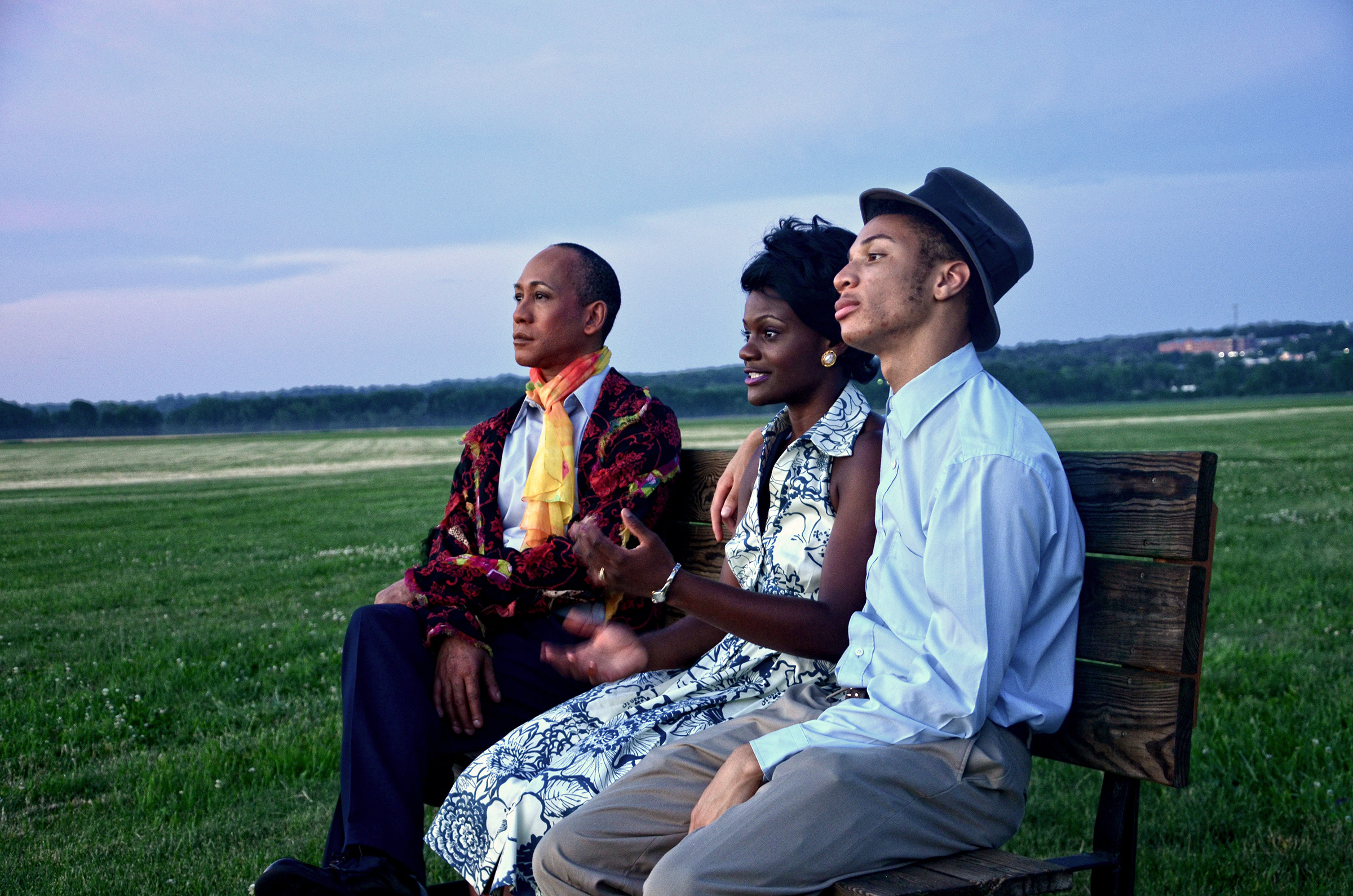 three people sitting on the bench in front of a sunset