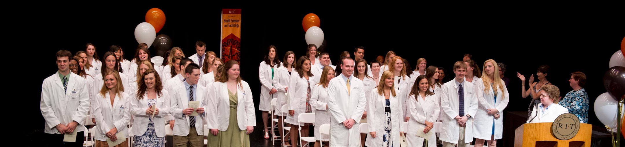 A class in white coats standing at a ceremony