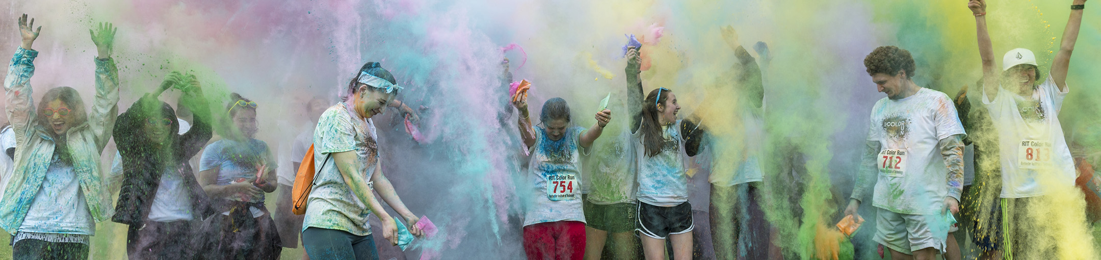 students in athletic wear stand under clouds of colored powder 