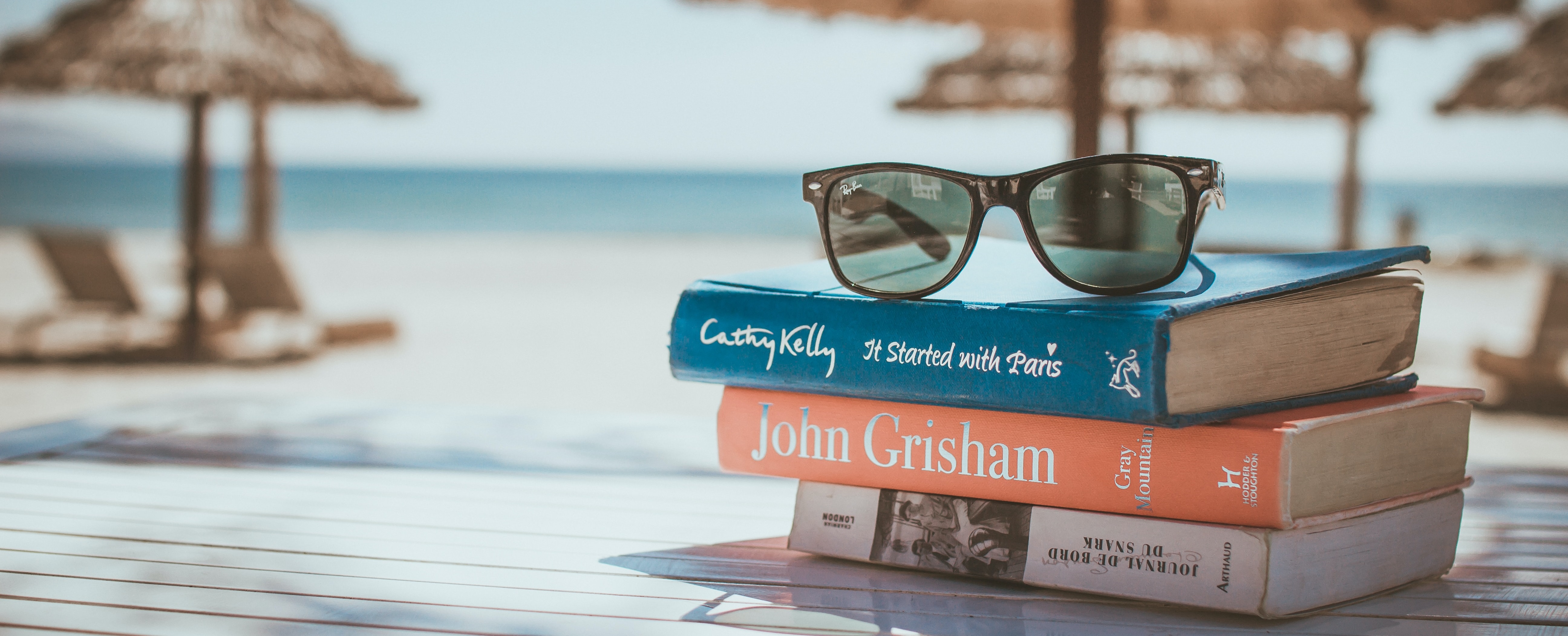 a beach scene featuring sunglasses atop a stack of books in the foreground