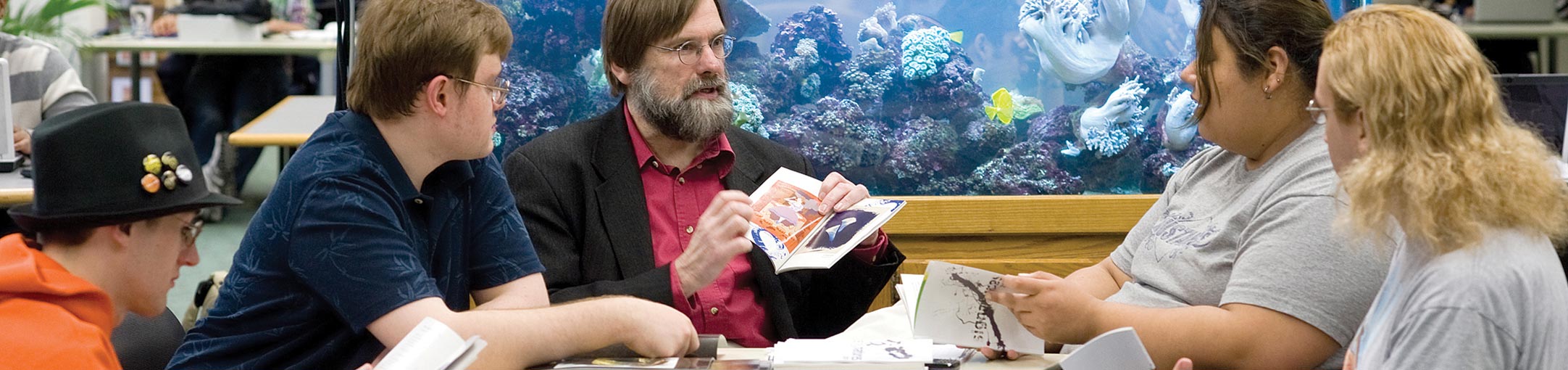A professor sitting with a small group of students with an aquarium behind him