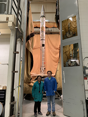 research student and faculty standing in front of a rocket