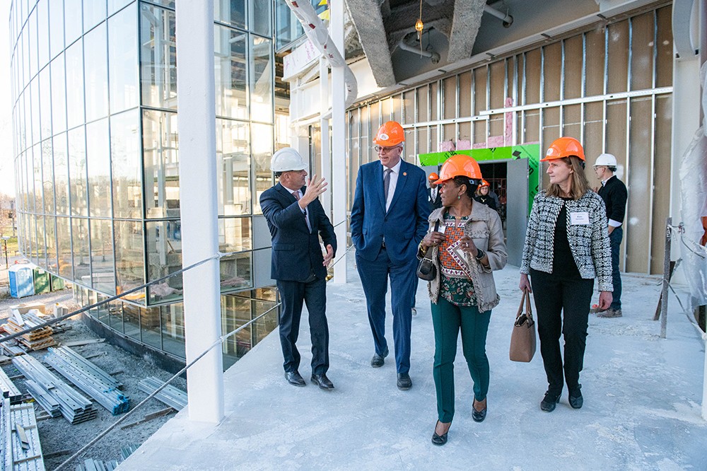 four people wearing hard hats walking in a building under construction.