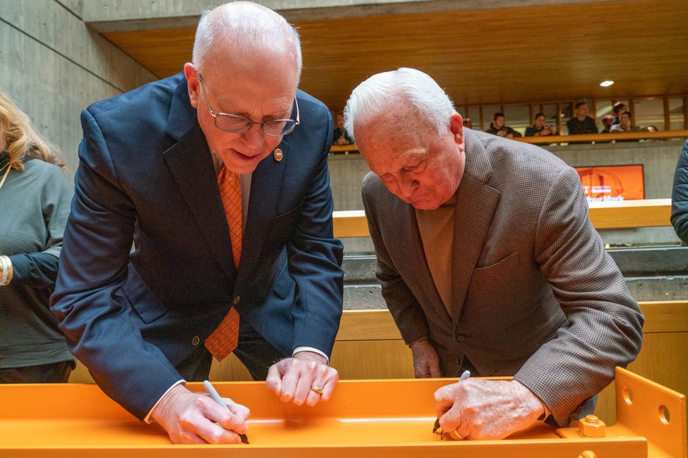 two men signing an orange steel beam.