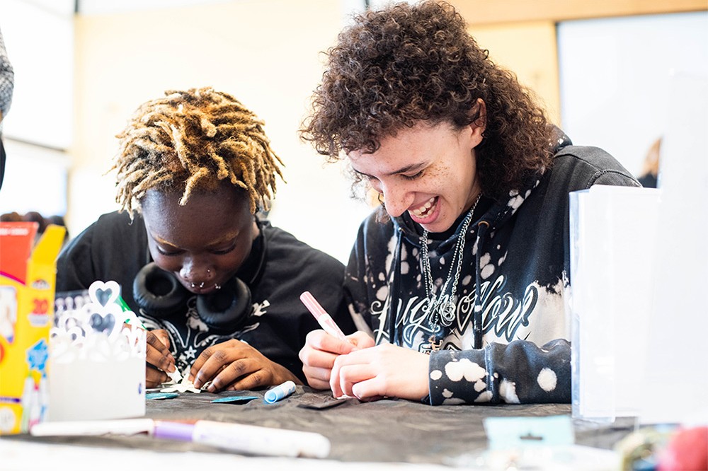 two college students smiling while coloring in flowers with markers.