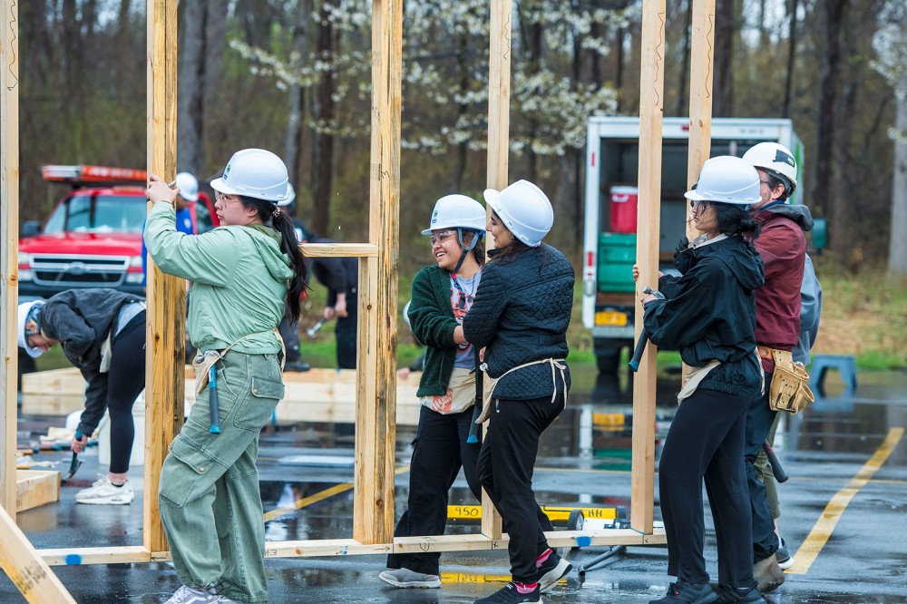 students are shown in hard hats raising the frame of a home for Habitat for Humanity.