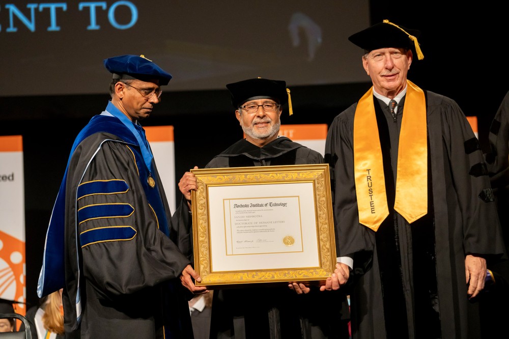 Sanjay Mehrotra stands on a stage holding an honorary degree.