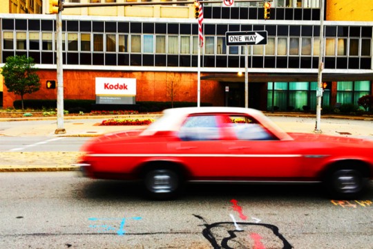 A blurry car motors by the Kodak building.