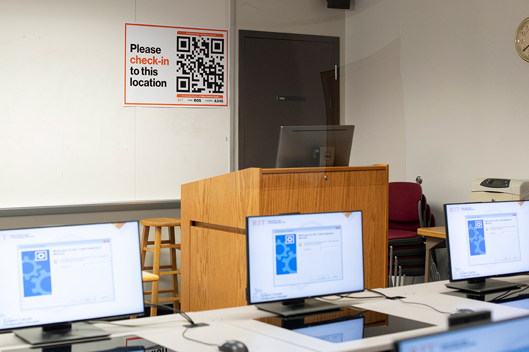 classroom with computers on a table and a poster with a Qr 