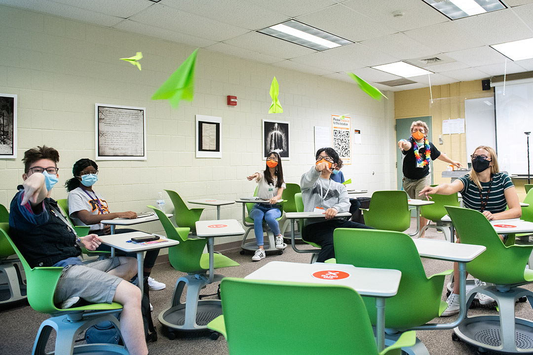 students in a classroom throwing paper airplanes.