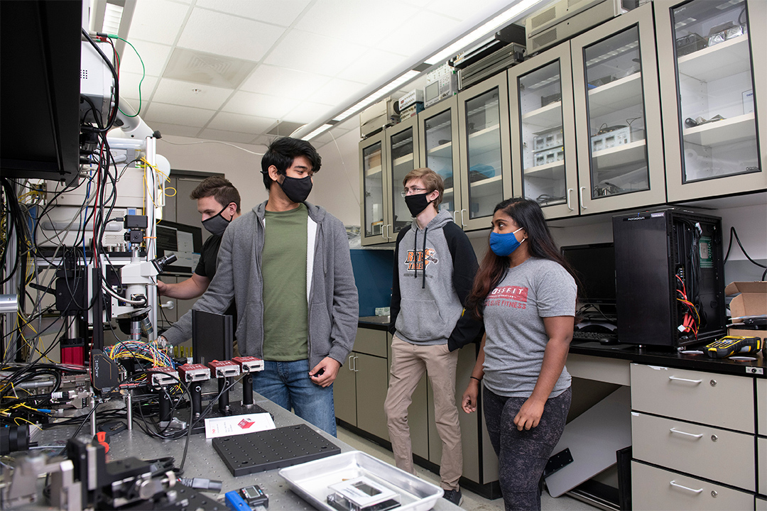four student researchers wearing masks in a quantum research lab.