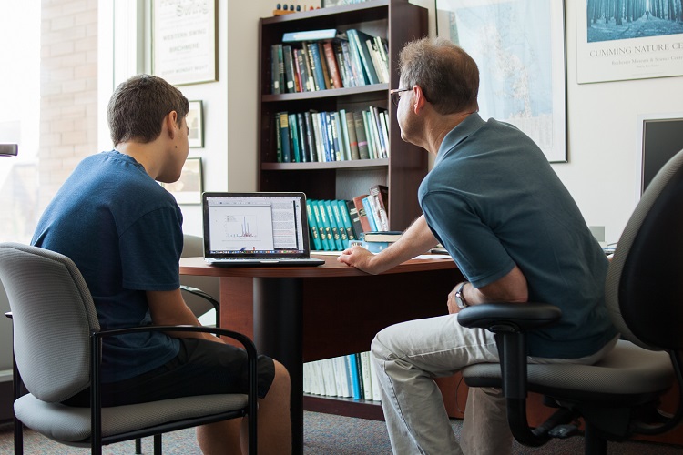 Student and instructor seated at a desk looking at a laptop