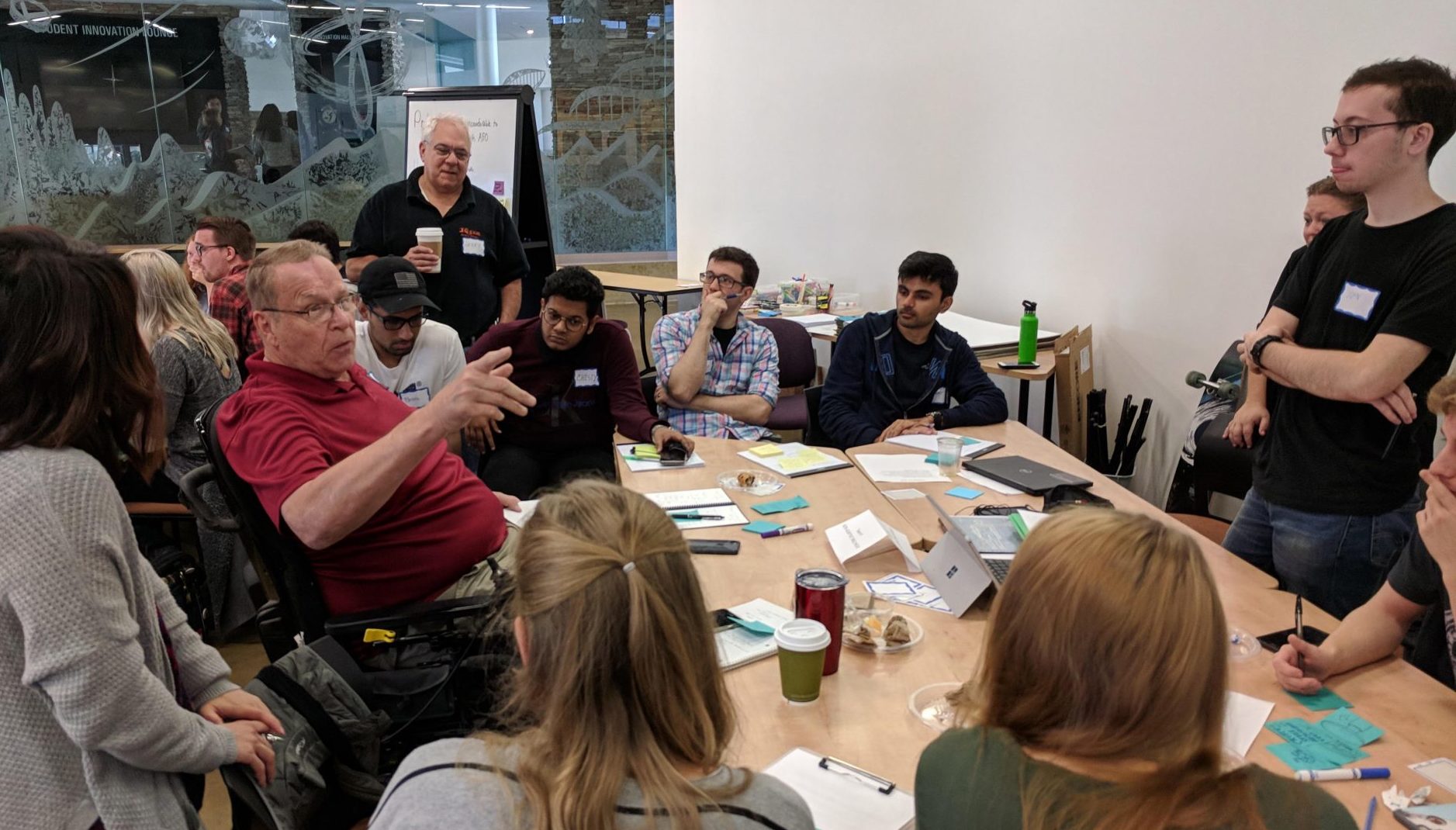 Students taking notes at an IdeaLab discussion with a man in wheelchair