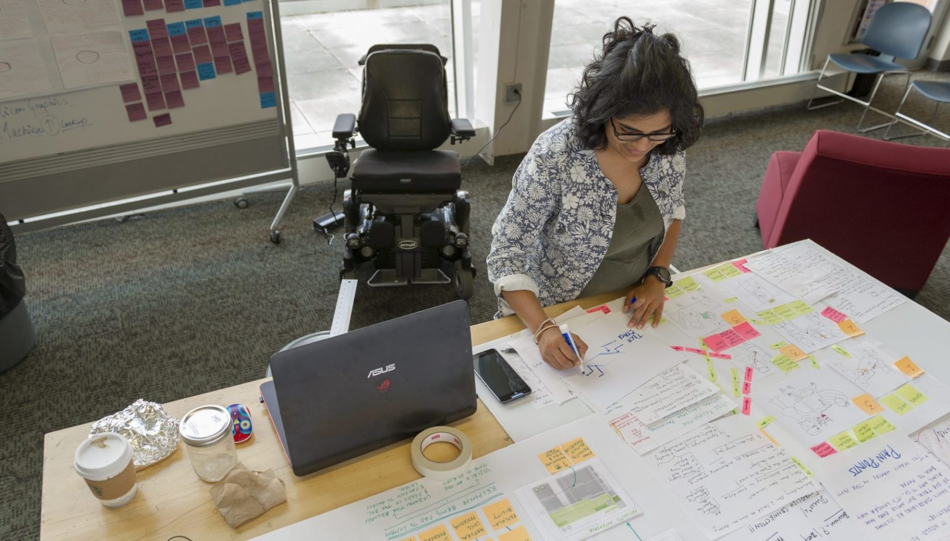 Woman at workstation table, papers with sticky notes cover the space