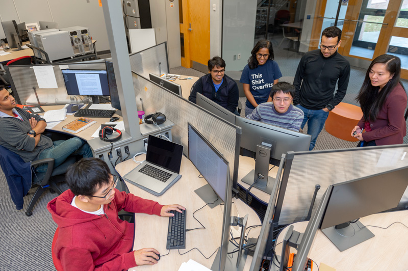students sit and stand talking to each other near a screen