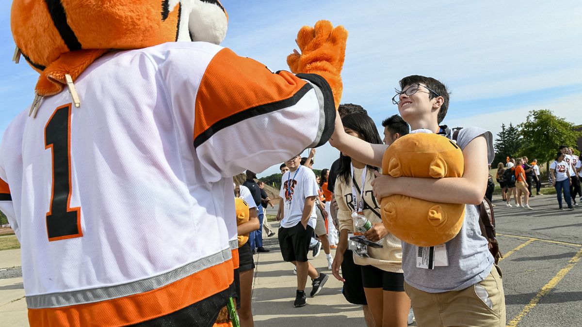 student giving the R I T tiger mascot a high-five.