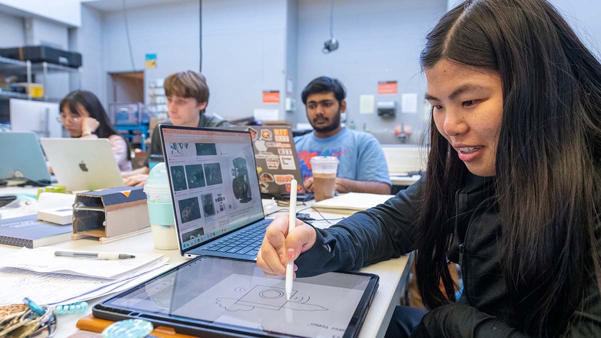 A group of students working collaboratively with laptops and tablets in a design lab.