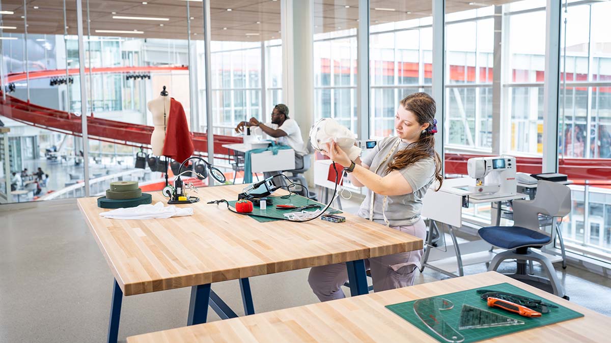 Students working with sewing equipment and materials in a bright, open makerspace.