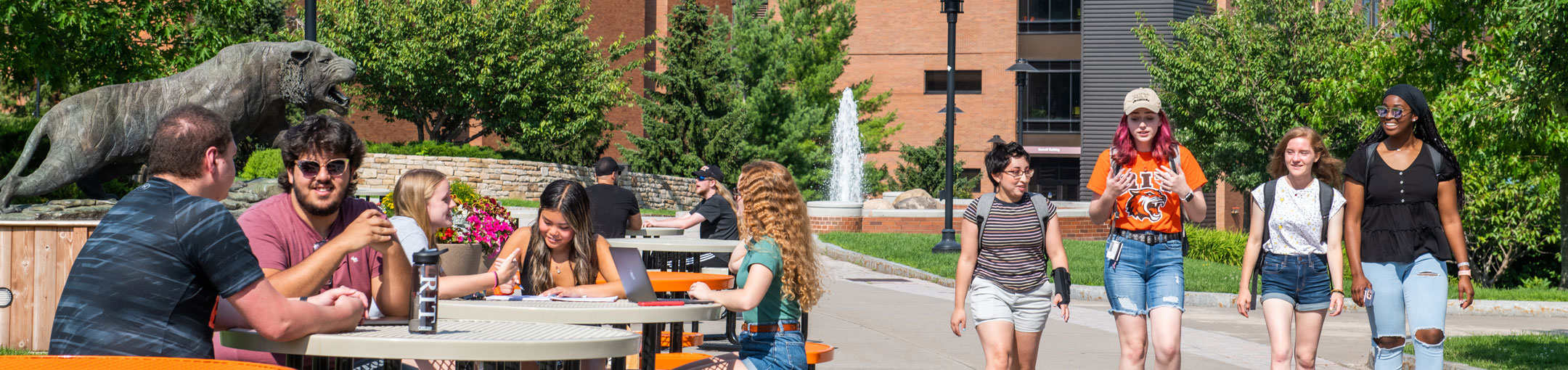 students walk past the RIT tiger statue while other students sit at a lunch table