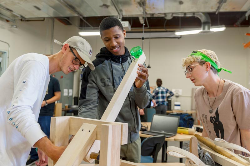 three students work on a wood engineering project in a lab