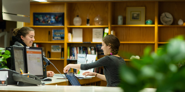 a student working at a desk interacts with another student