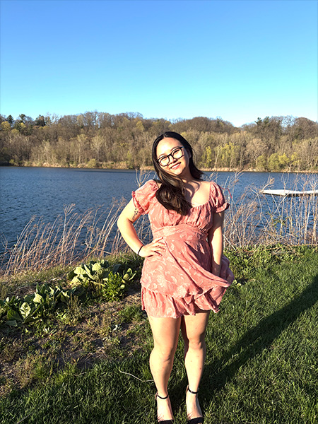 Student in front of lake in a pink dress