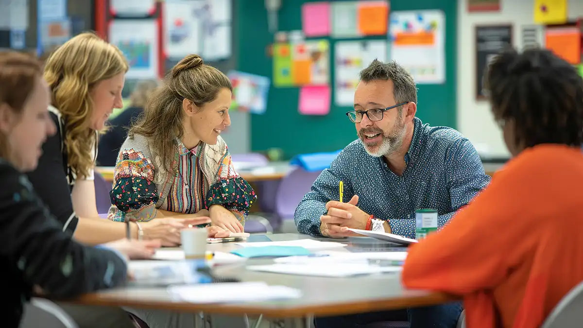 a group of professors having a meeting at a table in a classroom setting.