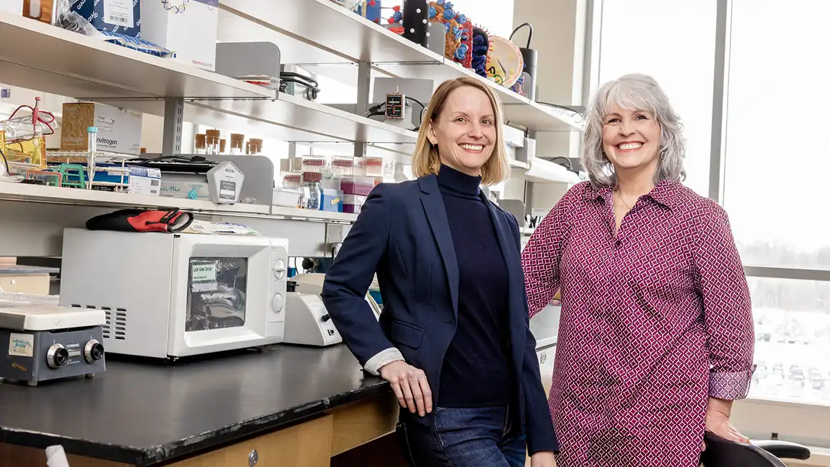 two researchers posing for a photo in a lab with beakers, scales, and other equipment.