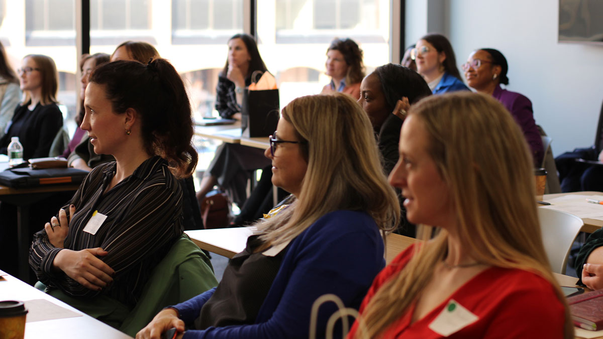 group of female faculty seated at long tables, listening to a presentation.