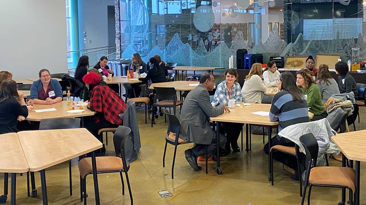 a group of faculty seated at hexagonal tables in a large gathering space.