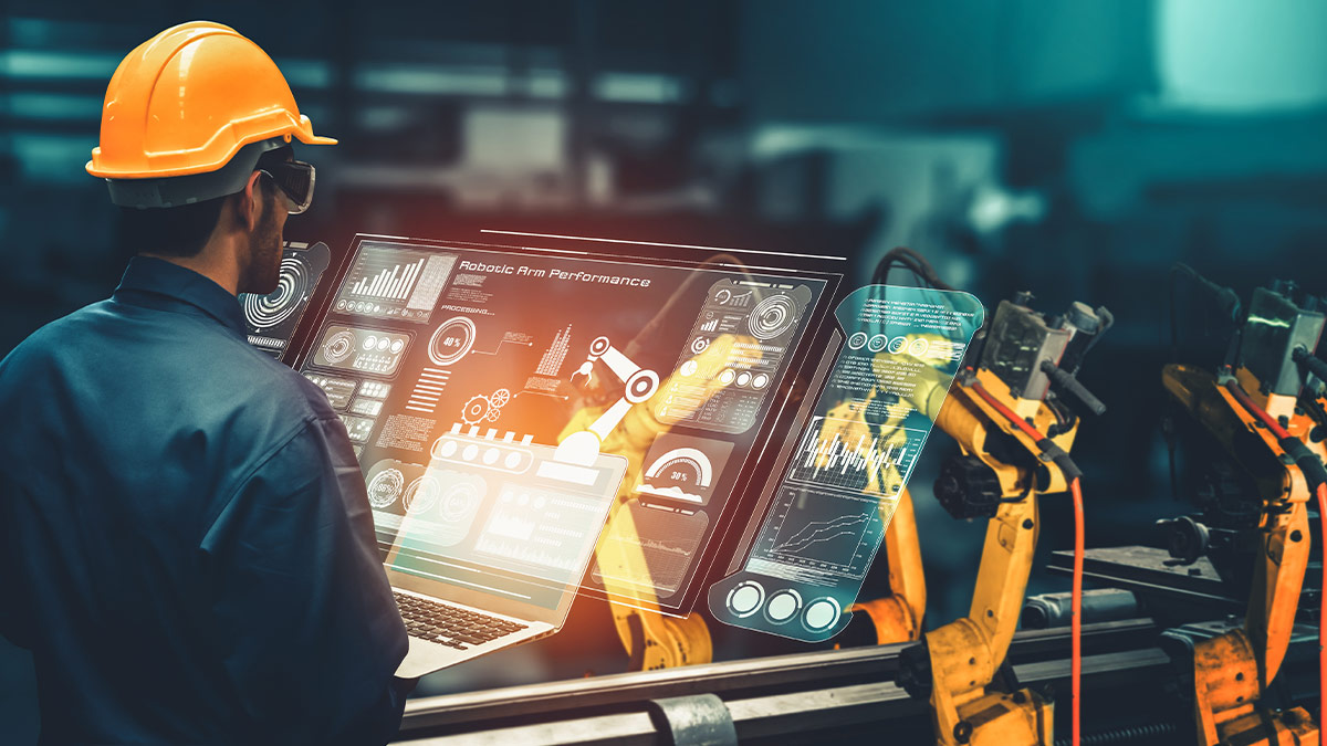 A worker in a hardhat looking at a futuristic monitoring display, with robotic arms in the background.