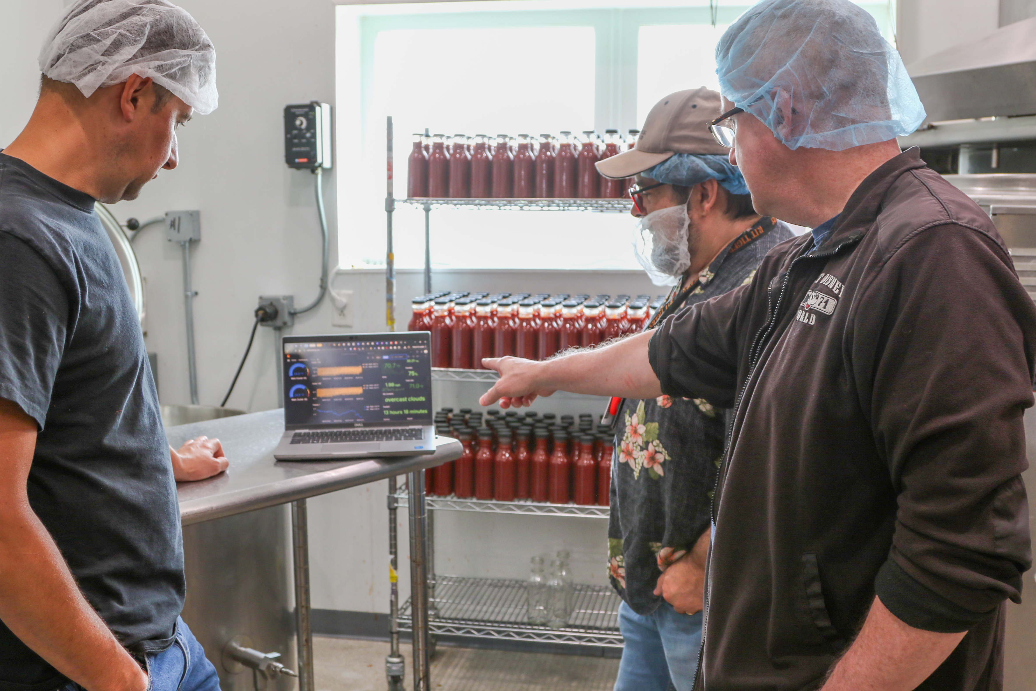 two engineers pointing to a laptop screen showing the temperature monitoring program to a worker