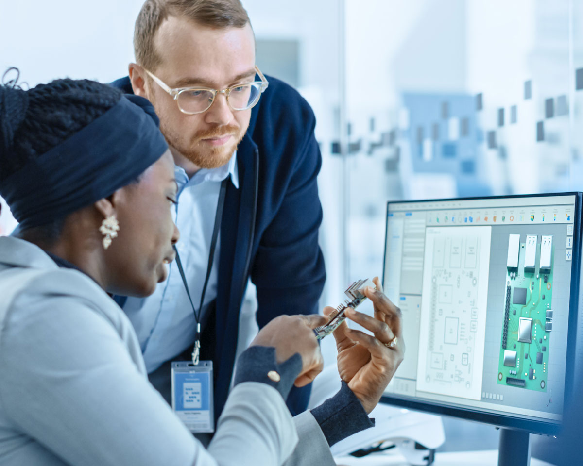 a man and woman at a computer holding a prototype part and looking at the screen