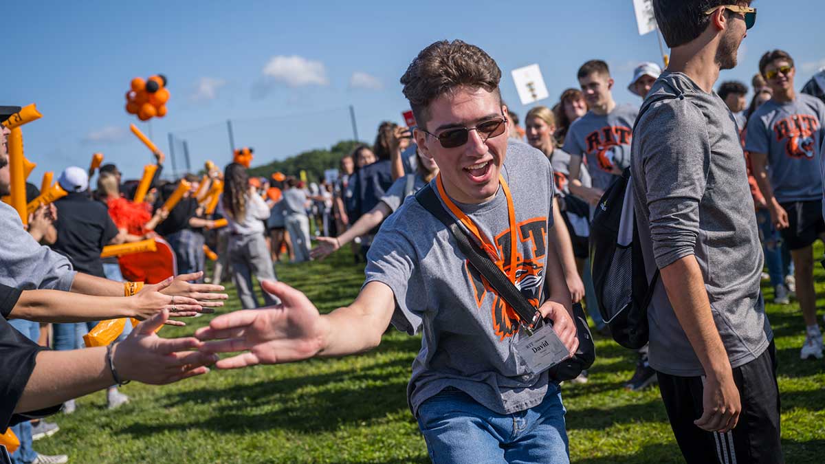 Excited student high-fives others while walking through a cheering crowd at a campus event.