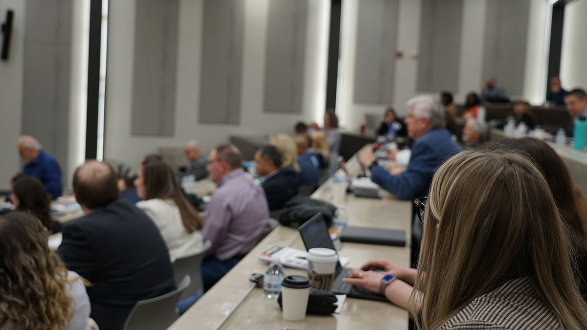 Audience members seated in a lecture hall, some taking notes or using laptops.