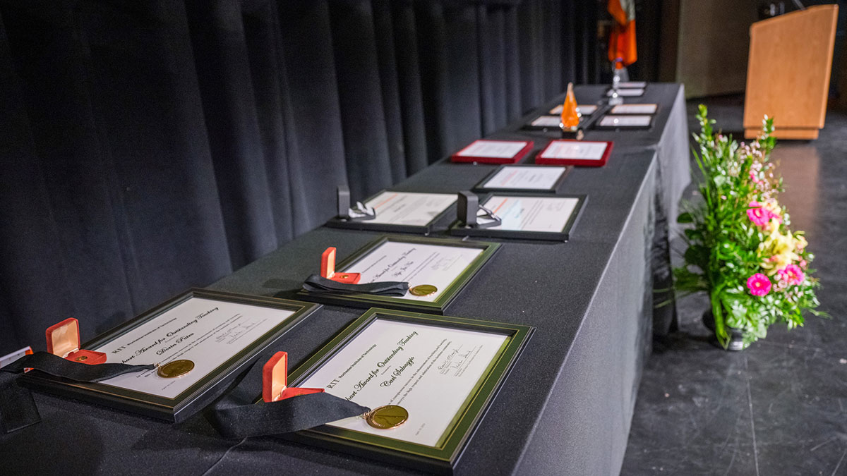 Row of framed award certificates and medals displayed on a black tablecloth at a ceremony.