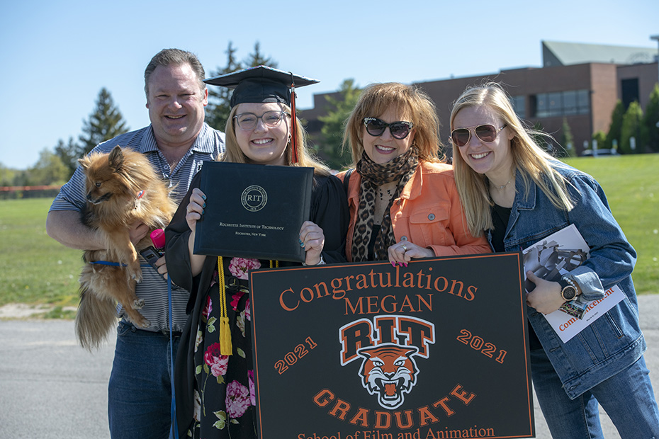 a graduate in cap and gown surrounded by three family members holding a congratulation sign.