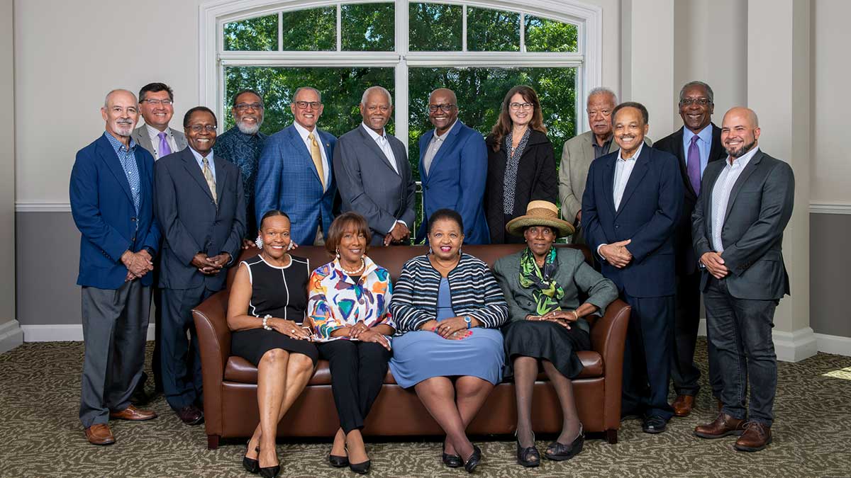 A large group of men and women pose together indoors in front of a large window.