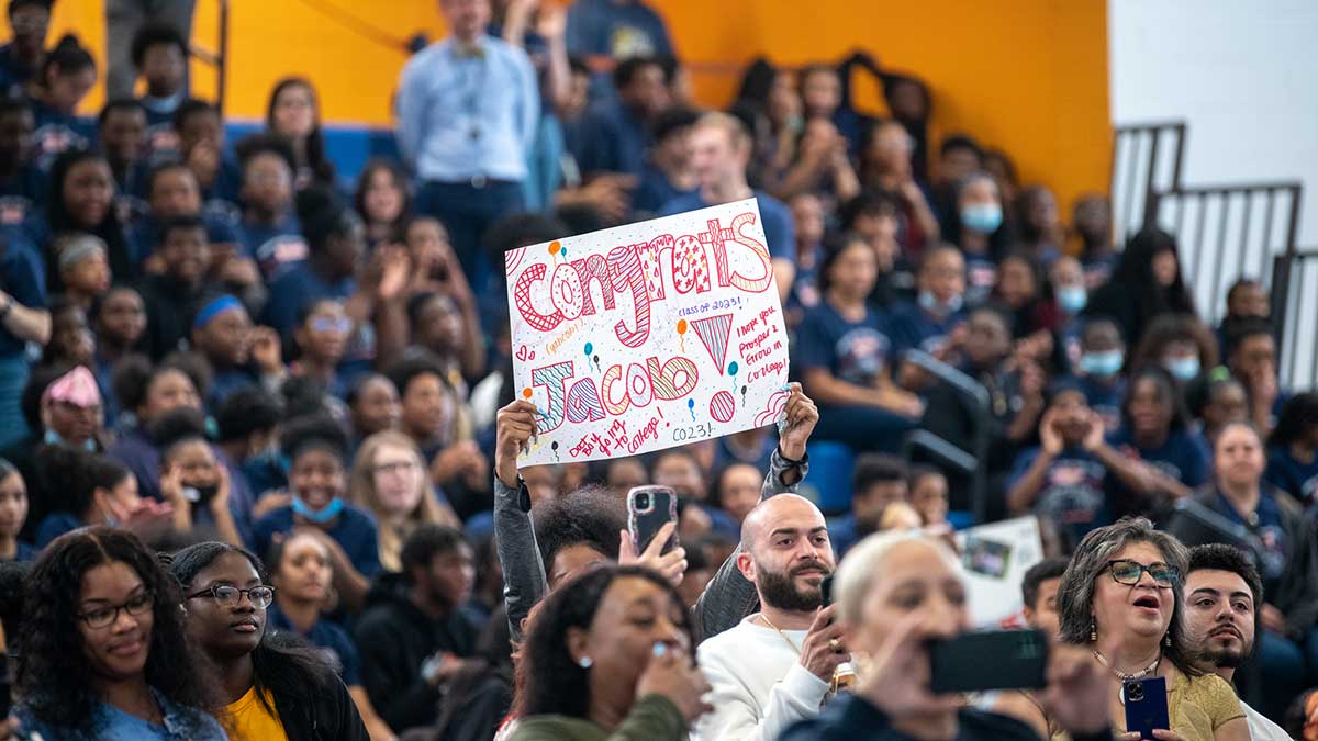 A crowd watches as someone holds a colorful 'Congrats Jacob' sign during a celebration event.
