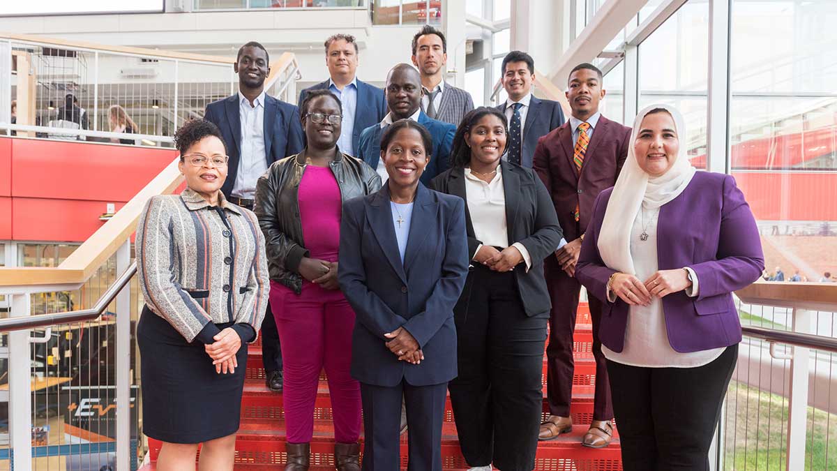 A diverse group in professional attire poses together on a red staircase inside a modern building.