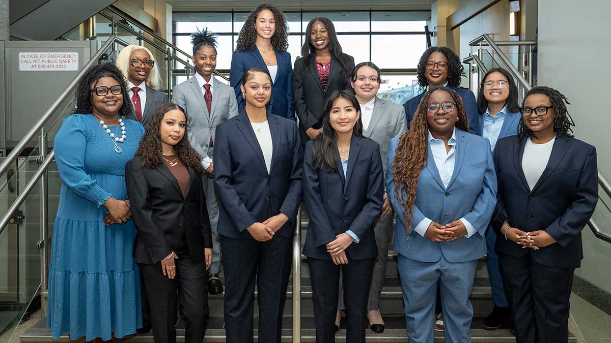 13 women in professional attire pose together on a staircase inside a modern building.