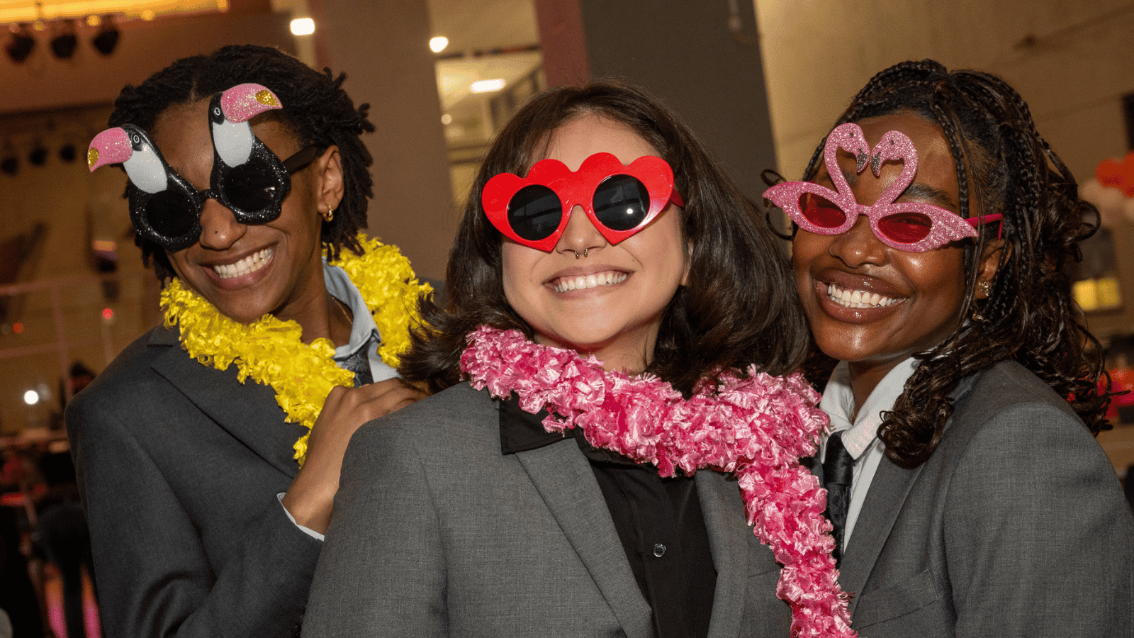 Three people wearing fun costume sunglasses smiling at the camera