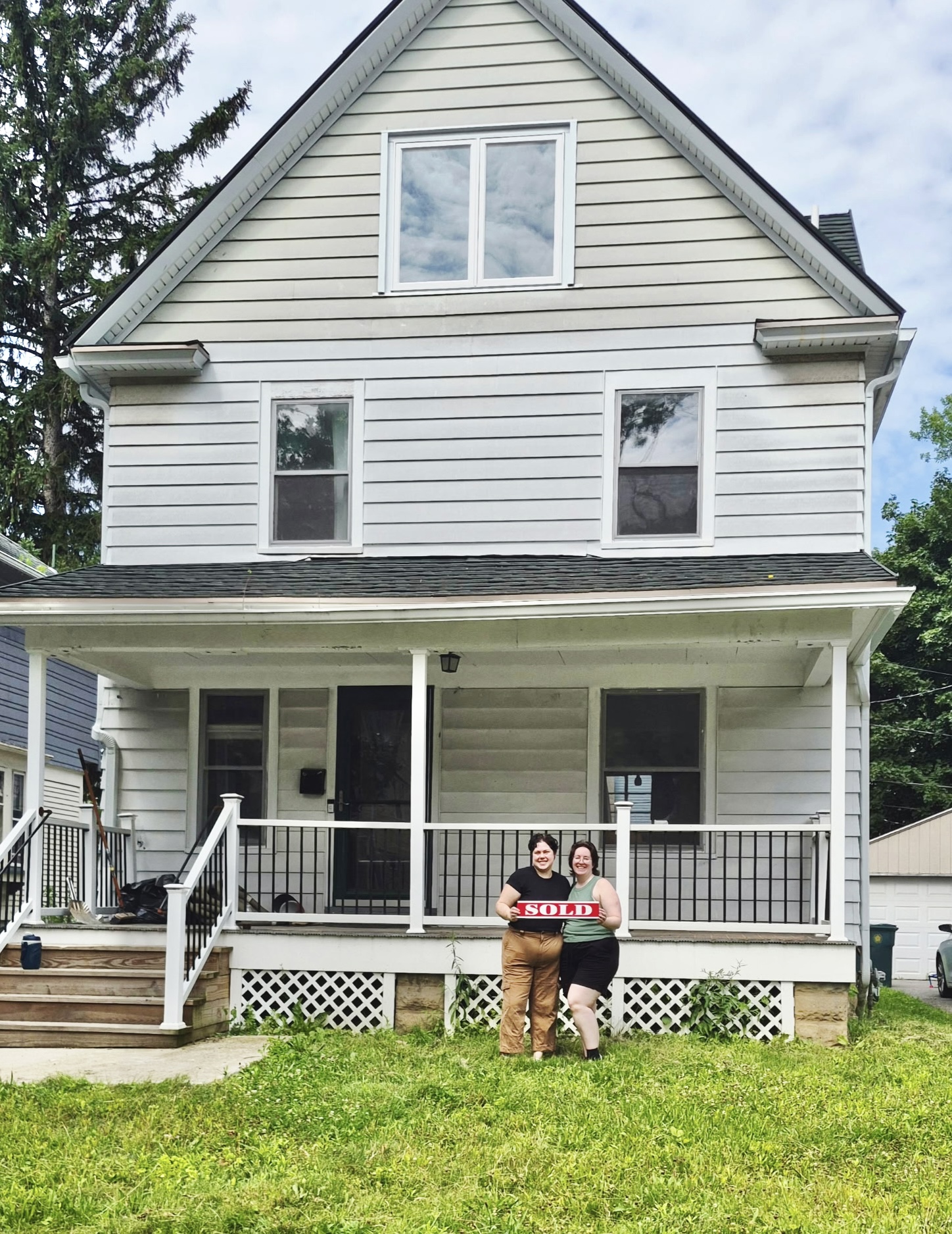 two people in front of a house holding a sold sign 